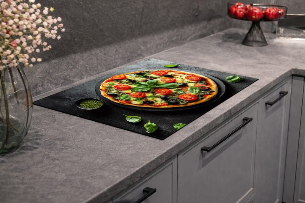 Afdekmat met een verse pizza met tomaat, mozzarella en basilicum op een zwarte achtergrond.